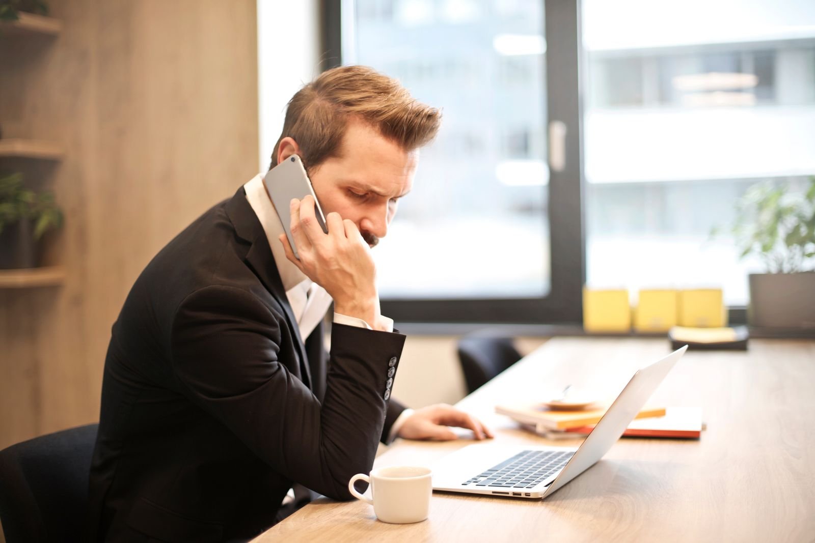 Businessman making a phone call while working on a laptop in a modern office