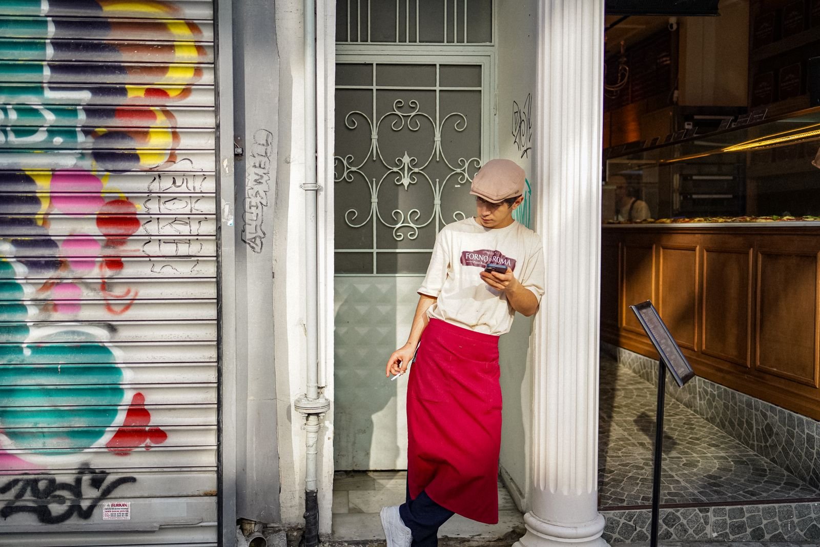 Young shop worker checking a phone outside a colorful local storefront