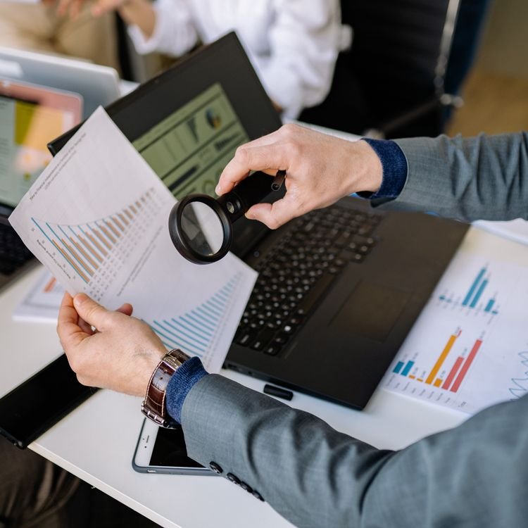 Businessman examining data charts with a magnifying glass over a laptop